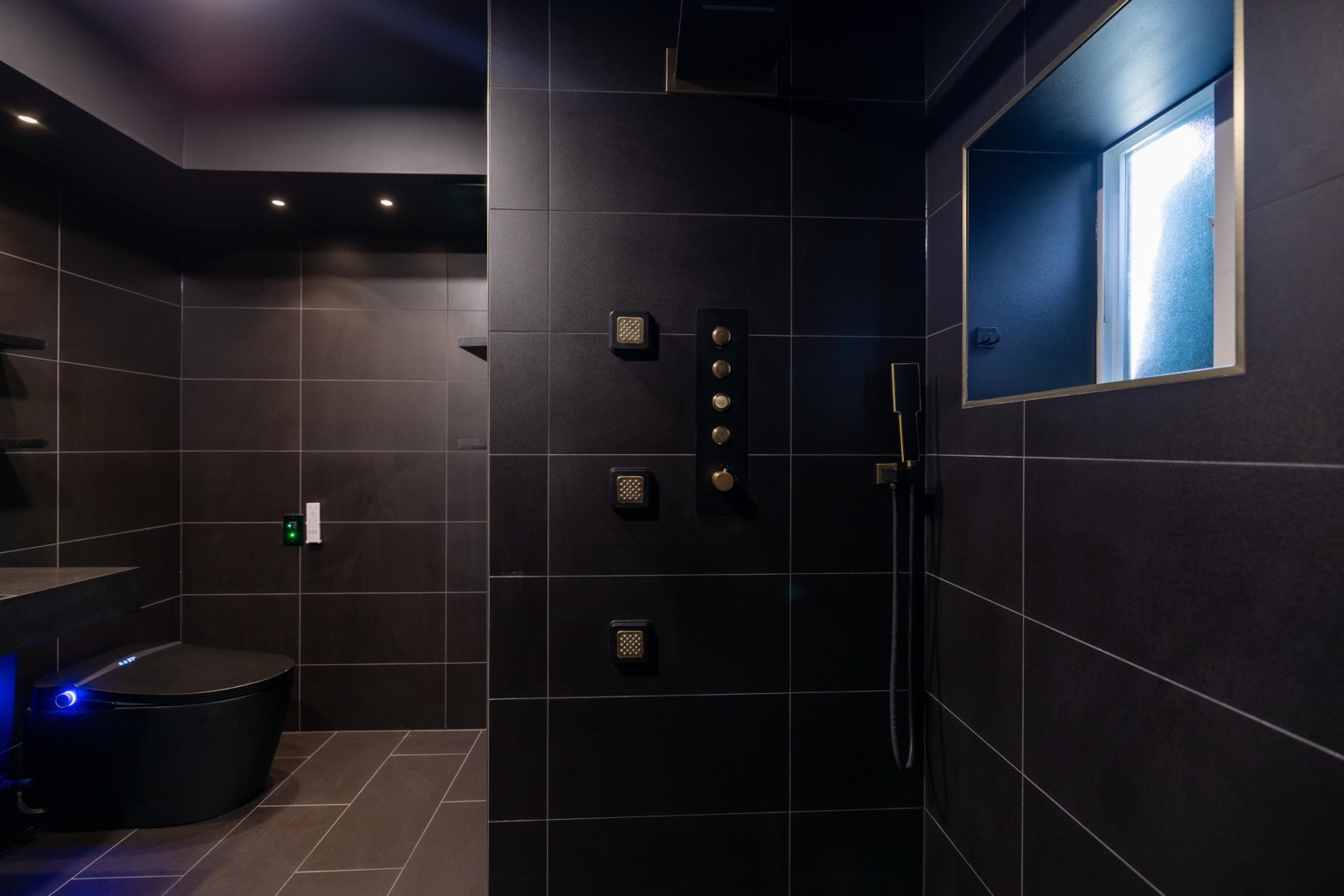 Dark tiled shower with multiple body sprays and a window