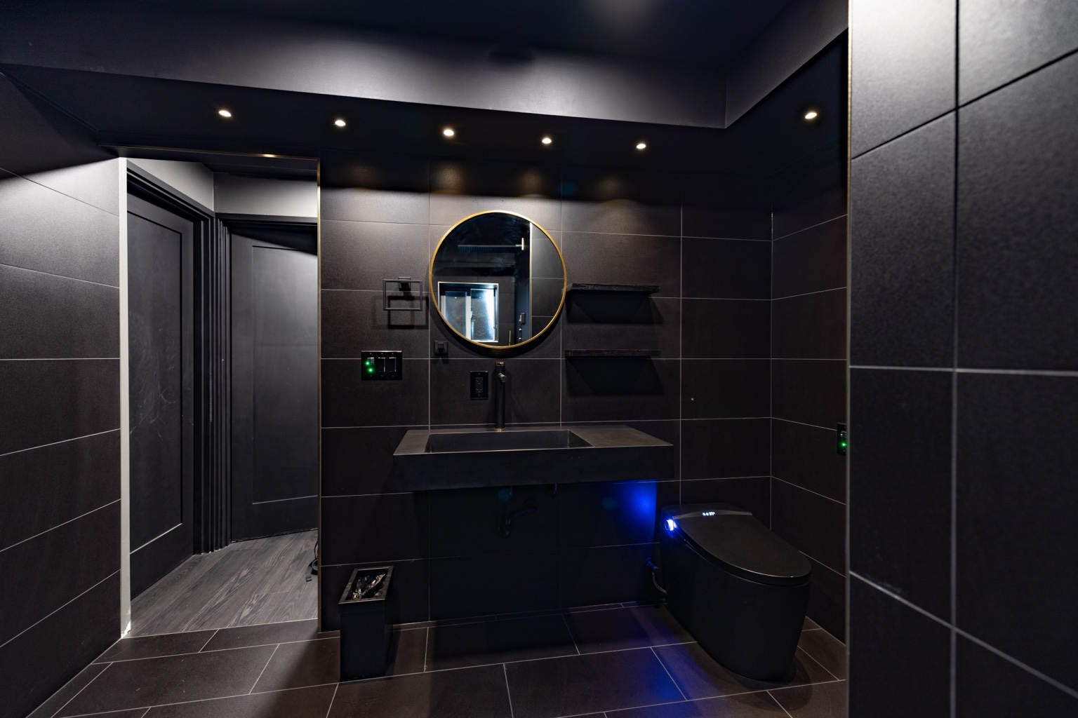 Dramatic charcoal bathroom with large wall tiles, a floating dark sink and a round gold-rimmed mirror