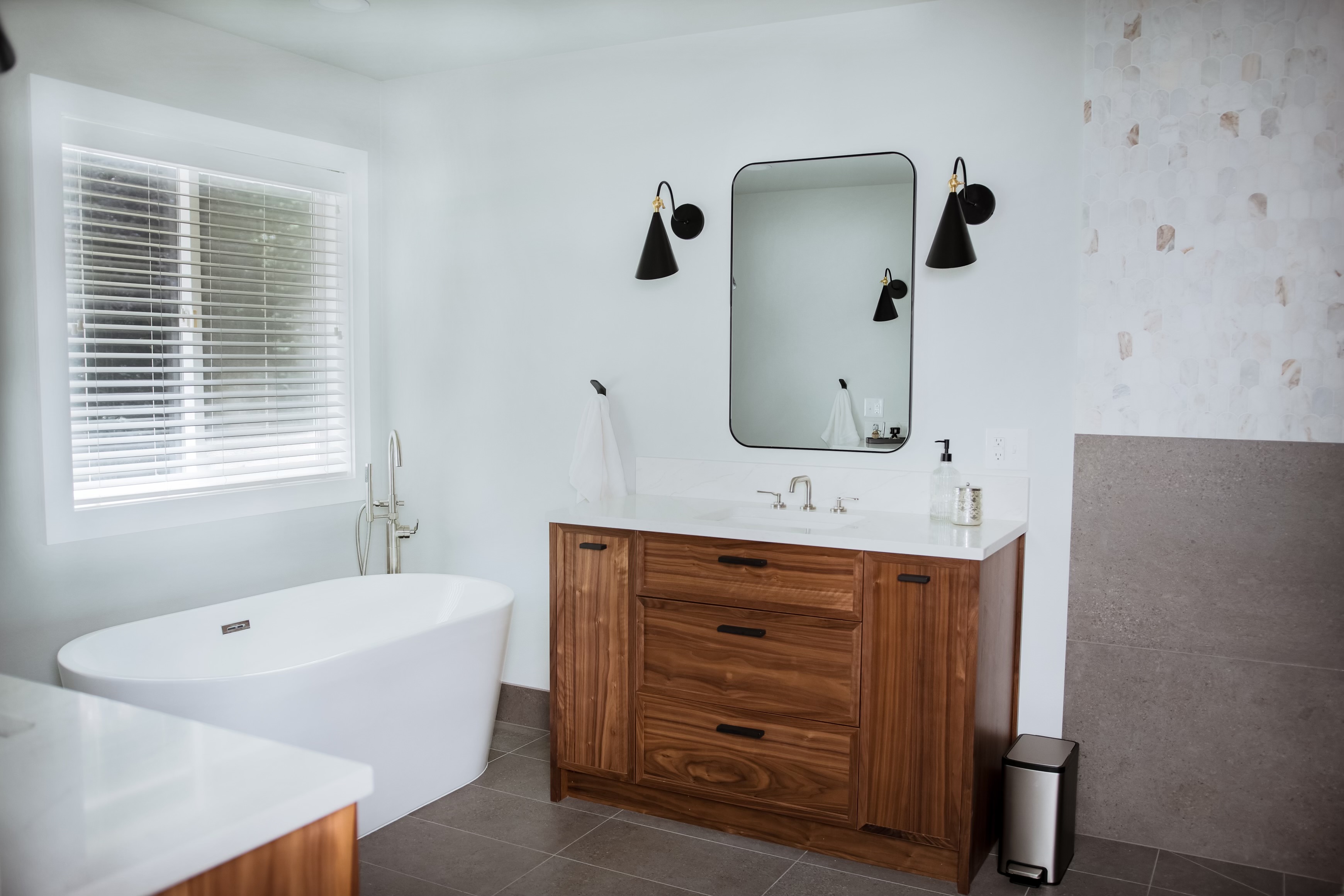 Bright bathroom with a freestanding white tub, natural wood vanity and black wall sconces