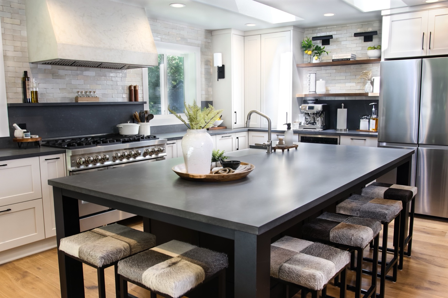 Light kitchen with a generous charcoal island, upholstered seating, pale cabinetry and natural wood shelves