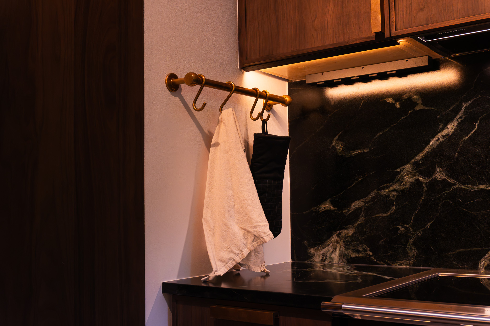 Wood cabinetry and a warm metal rail against a dark veined backsplash