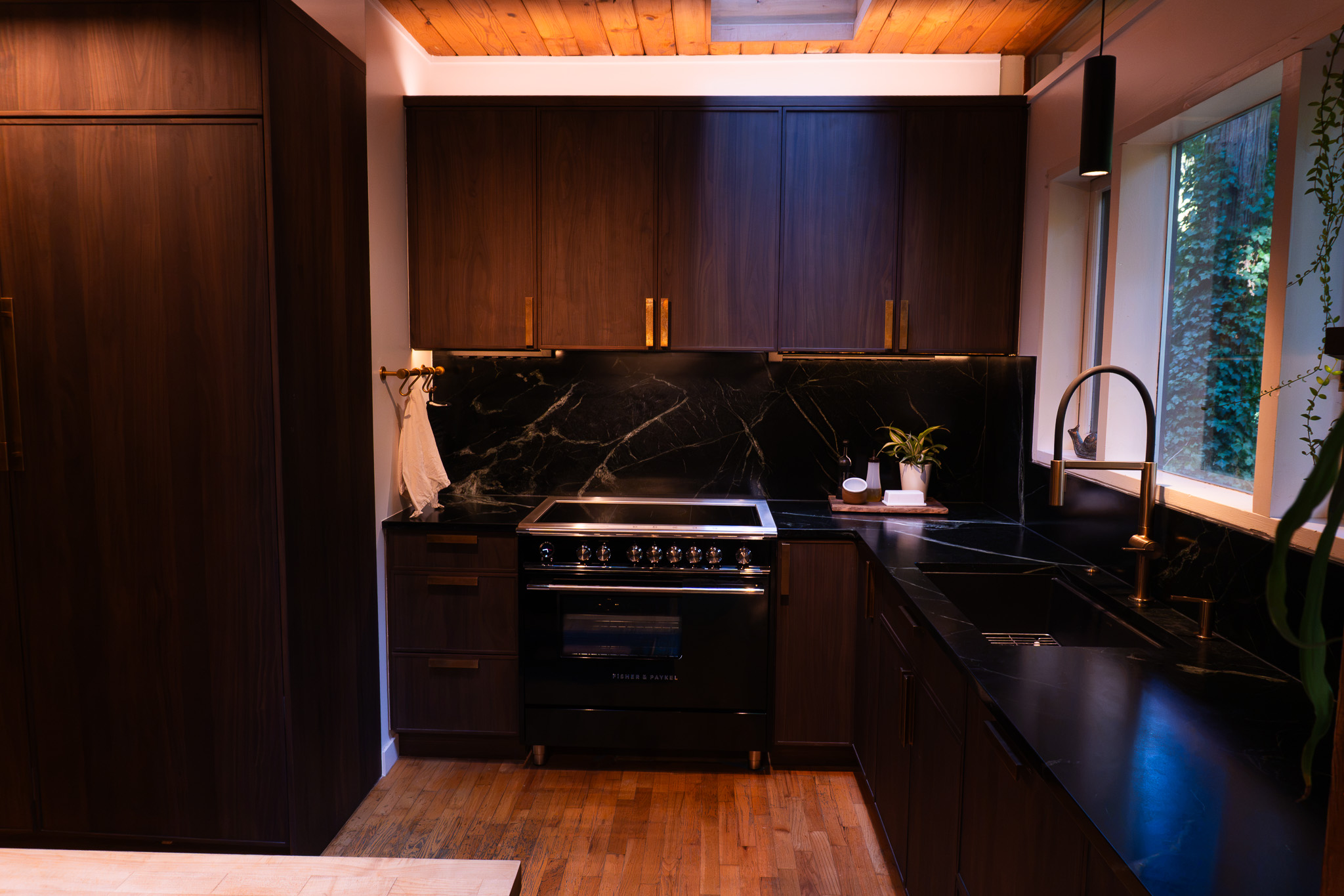 Rich wood kitchen cabinetry with dark veined surfaces, a black range and warm metallic fittings